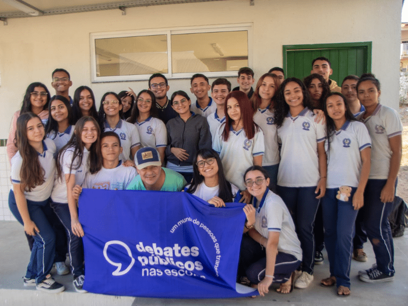 Grupo de estudantes posando para a foto. Ao centro, algumas pessoas seguram a bandeira dos Debates Públicos
