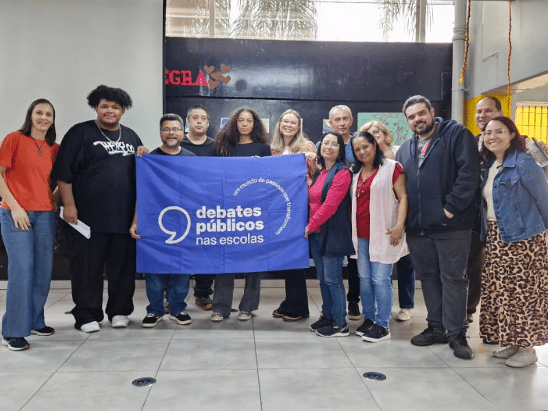 Grupo de pessoas reunidas posando para a foto segurando a bandeira dos Debates Públicos