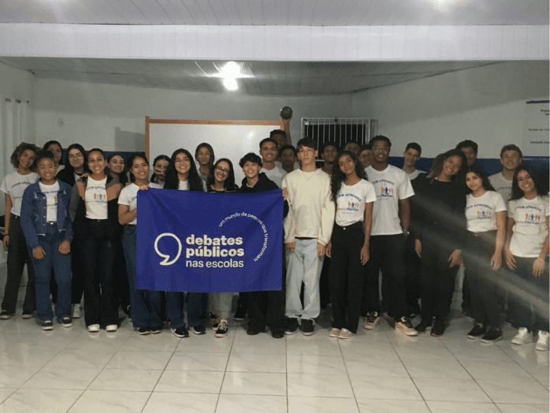 Grupo de jovens reunidos em uma sala de aula exibindo a bandeira dos Debates Públicos